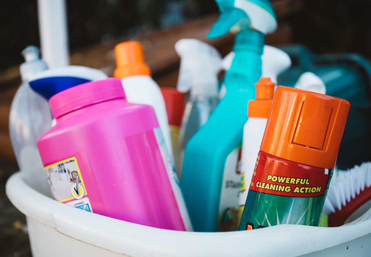 services-img Close-up of assorted cleaning supplies in a bucket outdoors, showcasing various detergents and sprays.